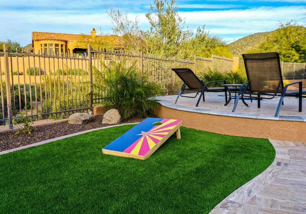 A Palm Springs-inspired mini-golf course on a ship deck features holes marked by white flag poles. The green artificial turf, installed by a professional Artificial Turf Installer, complements ship railings and deck chairs in the background. Two lantern-style lights add charm to the scene.